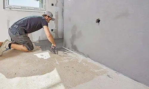 Ein Mann spachtelt aus der Dusche heraus den eigentlichen Badboden in einem Zug.