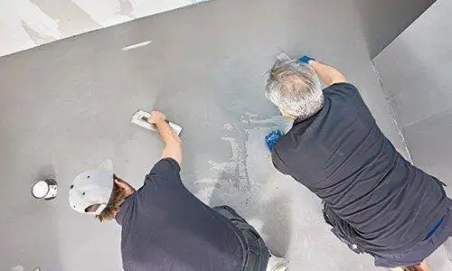 Zwei Männer bespachteln und verpressen die Spachtelmasse auf dem Badezimmerboden.