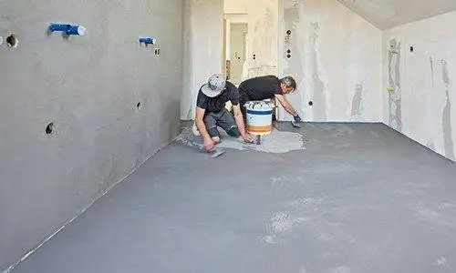 Zwei Männer bespachteln und verpressen die Spachtelmasse auf dem Badezimmerboden.