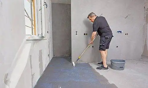 Imprägnierung des Badezimmerbodens mit einer Rolle von einem Mann.