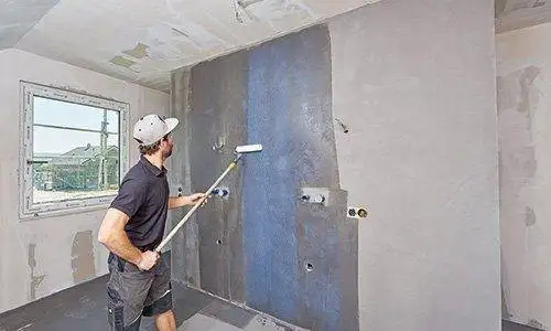 Ein Mann imprägniert die Badezimmerwand mithilfe einer Rolle am Teleskopstab.