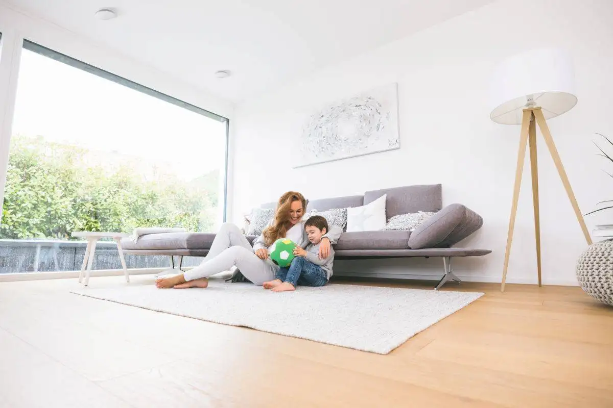 Küche renovieren: Jetzt in 4 Schritten renovieren 7 Mutter sitzt mit Sohn im WOhnzimmer auf einem Teppich. Im Hintergrund zu sehen: eine große Fensterfront und ein kleines Sofa