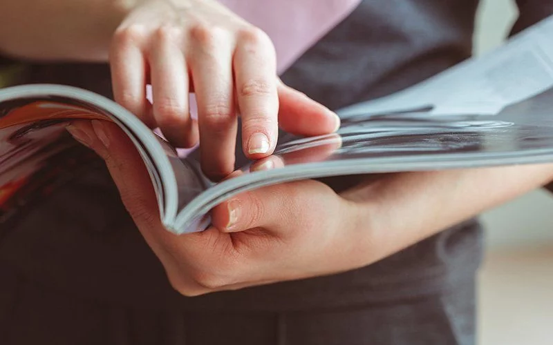 Shop 2 Abonnement. Eine Frauenhand fährt mit dem Finger über eine Seite in der Zeitschrift.