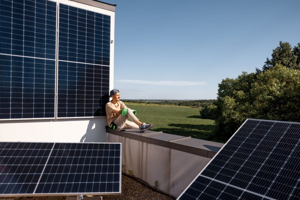 Solaranlagen auf einem Balkon, ein Mann sitzt auf der Brüstung seines Balkons.