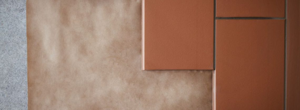 Estrichziegel Verarbeitung und Vorteile im Zusammenspiel mit Fußbodenheizungen: Estrich am Boden, darüber sind terrakottafarbene Fliesen, die versetzt angebracht sind.