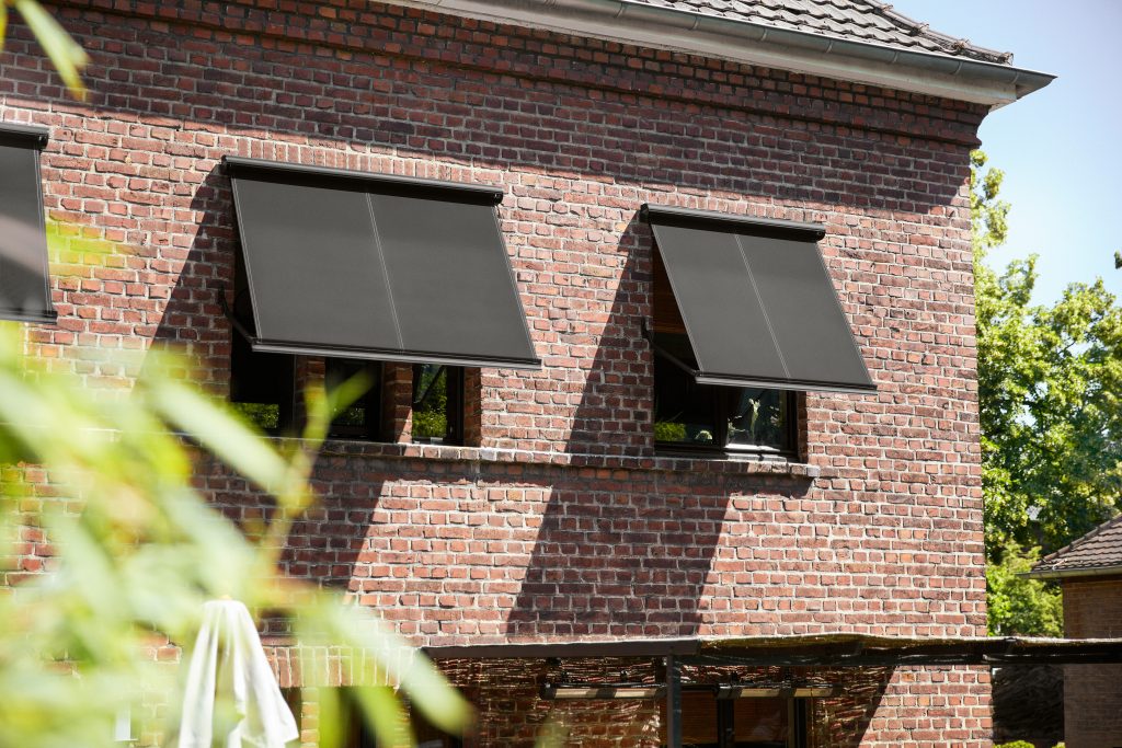 Klinker-Fassade mit drei Fenstern, die mit Sonnenschutz aus anthrazit-farbenem Material ausgestattet sind. Warema Sonnenschutz Markise