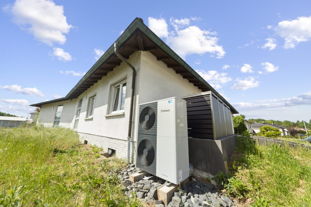 Vor einem einstöckigen Bungalow steht eine Wärmepumpe.