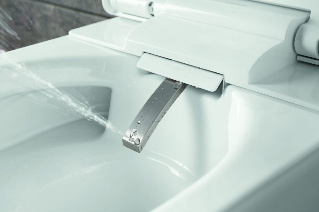 Traumbäder ohne Grenzen 5 Nahaufnahme eines weißen Dusch-WCs mit ausgefahrenem Duscharm aus Edelstahl, aus dem ein präziser Wasserstrahl austritt.