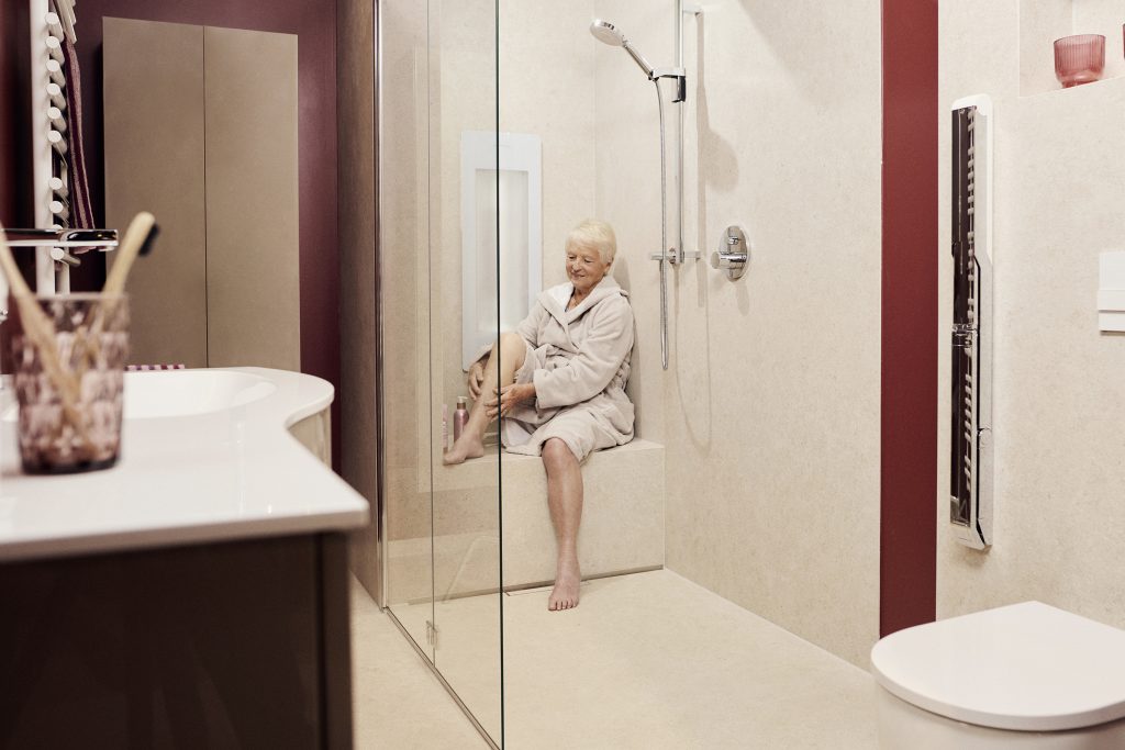 Traumbäder ohne Grenzen 7 Eine Seniorin sitzt entspannt in einer modernen, barrierefreien Dusche mit gemauerter Sitzbank.